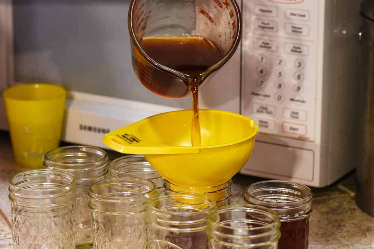 pouring cooked apple jelly from juice into half pint jelly jars for canning, using yellow canning funnel