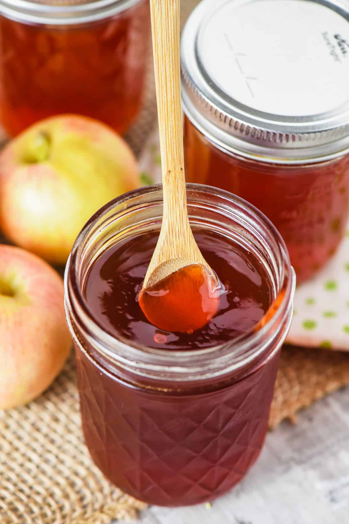 small wooden spoon in half pint jar of apple jelly with Gala apples