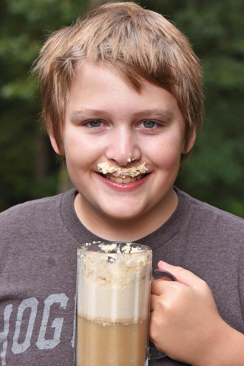 boy drinking butterbeer recipe from glass mug with whipped cream mustache