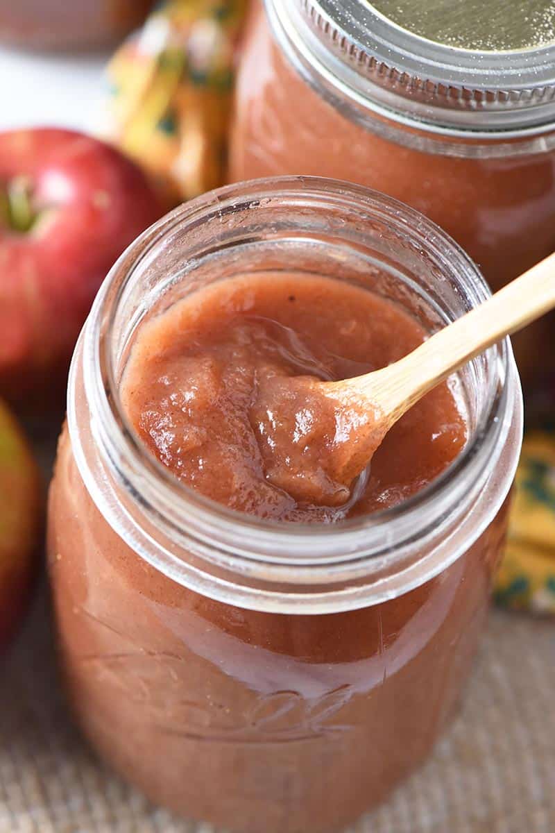 cinnamon applesauce in Ball canning jar with small wooden spoon and fresh apples