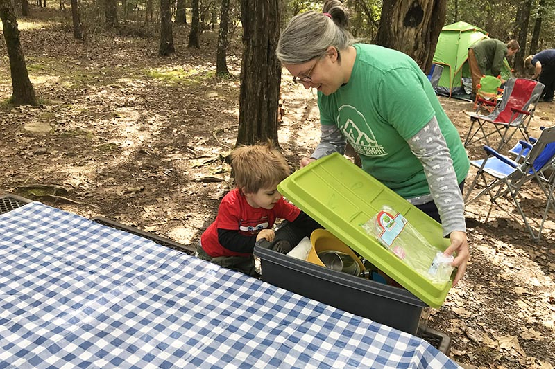 mom and toddler getting camping cooking gear on Petit Jean State Park campground picnic table in campsite