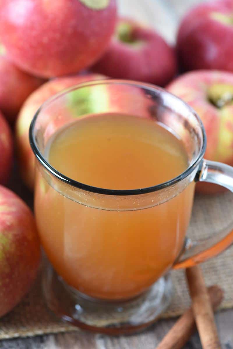 hot apple cider, mulled cider, in a glass mug with apples and cinnamon sticks
