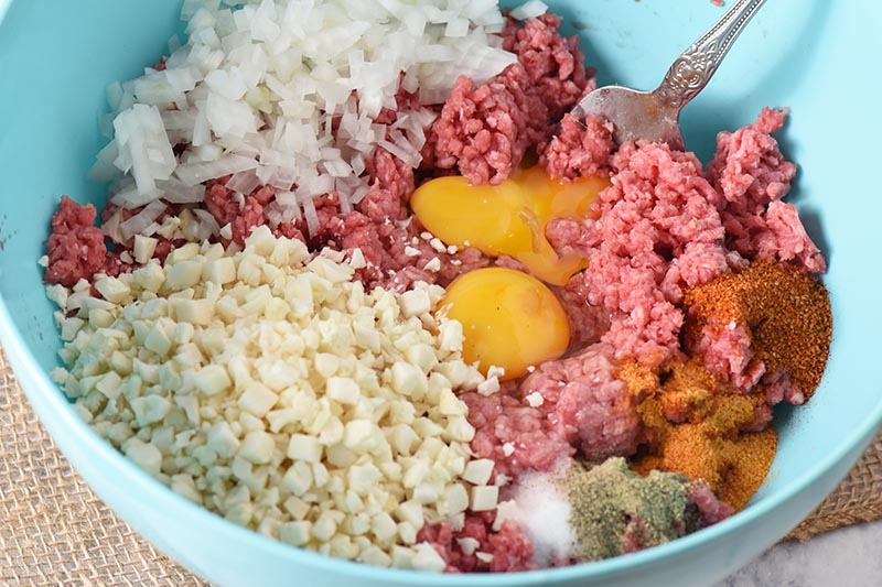 low carb meatloaf ingredients in blue mixing bowl, including ground beef, cauliflower rice, onion, eggs, and seasonings