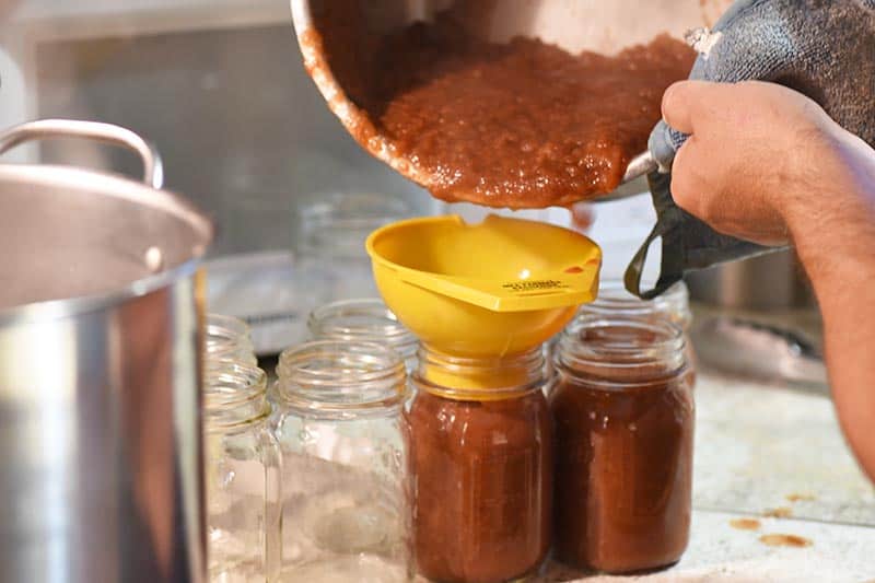 pouring cinnamon applesauce through funnel into canning jars