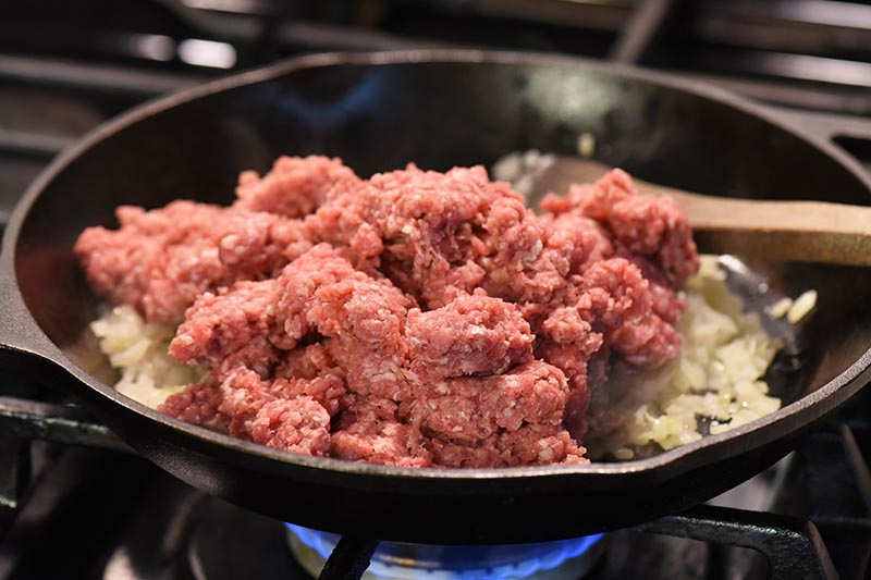 adding ground beef to sloppy joes mixture with onions and garlic in cast iron skillet
