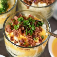 mashed potato bar, including mashed potato cup with bacon, cheese sauce, and chives, with spoon in ready to eat