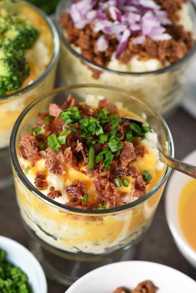 mashed potato bar, including mashed potato cup with bacon, cheese sauce, and chives, with spoon in ready to eat