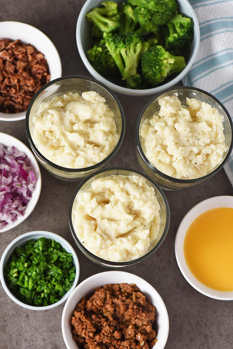 mashed potatoes with mashed potato bar toppings on gray countertop with white and blue kitchen towel