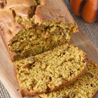 sliced loaf of homemade pumpkin bread on a wooden cutting board with a decorative pumpkin
