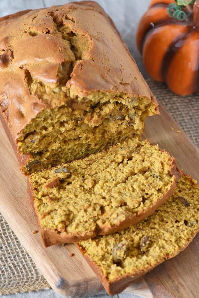 sliced loaf of homemade pumpkin bread on a wooden cutting board with a decorative pumpkin