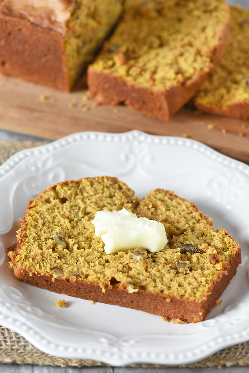 slice of moist pumpkin spice bread with butter on white plate