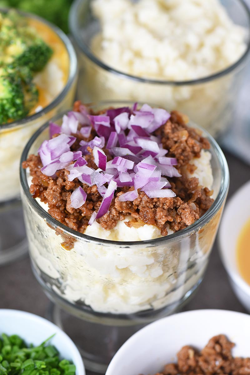 sloppy joe meat and red onions on mashed potato in small glass trifle dish