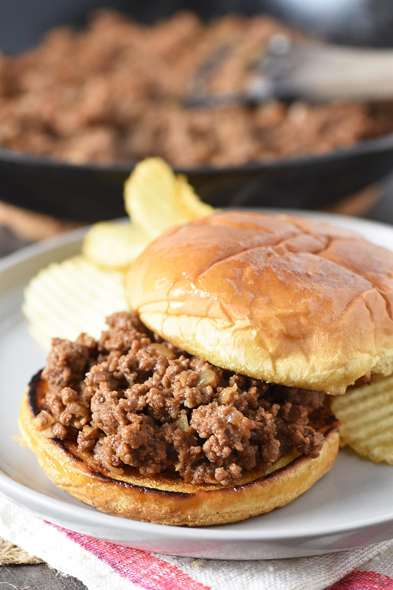 open faced sloppy joes with potato chips on gray plate and sloppy joe meat in iron skillet