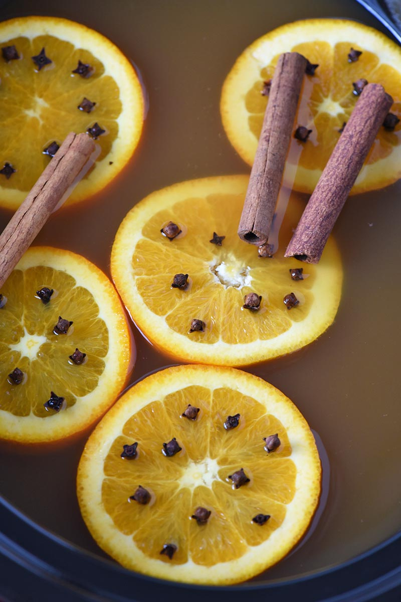 slow cooker mulled cider with orange slices, whole cloves, and cinnamon sticks