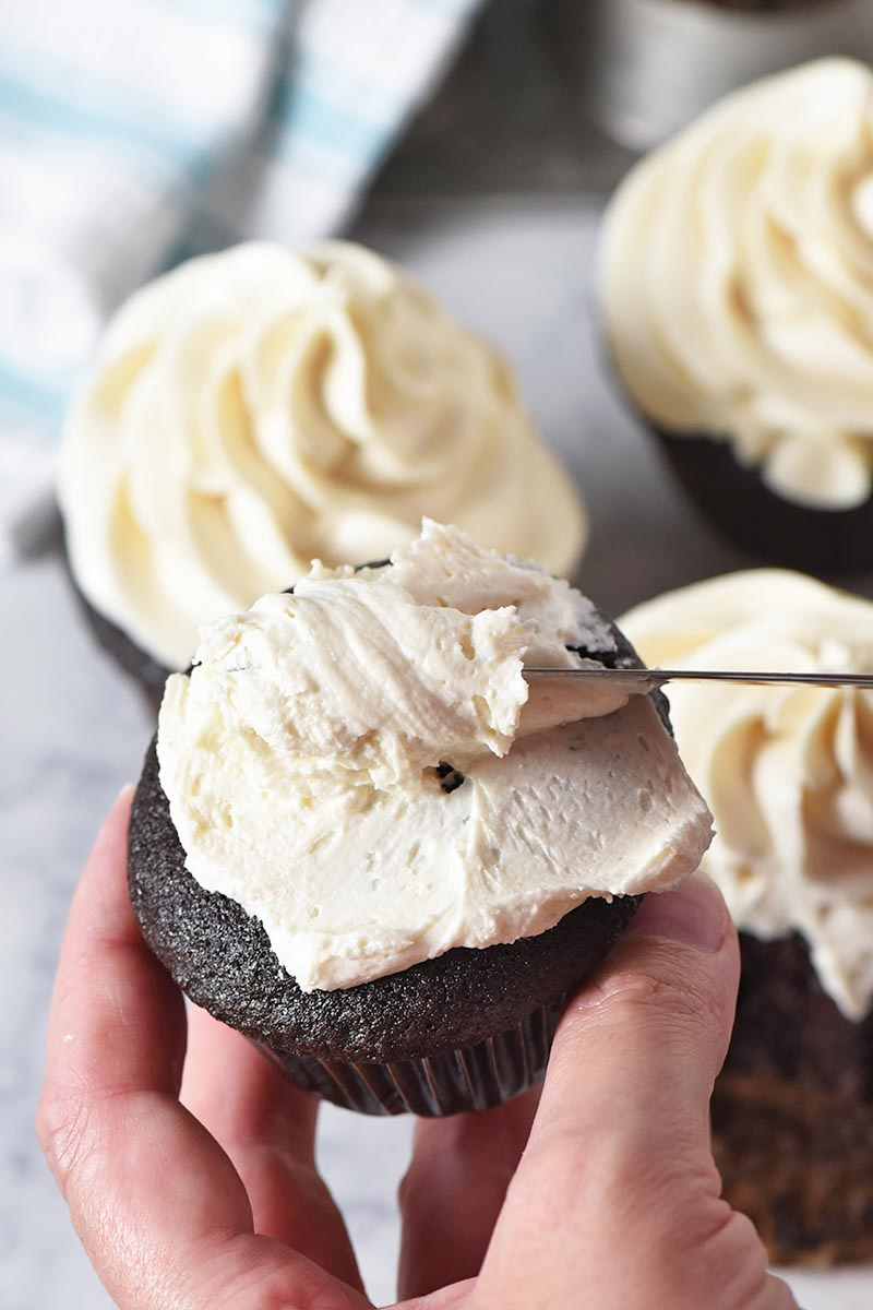 spreading butterbeer buttercream frosting onto dark chocolate cupcakes with a table knife