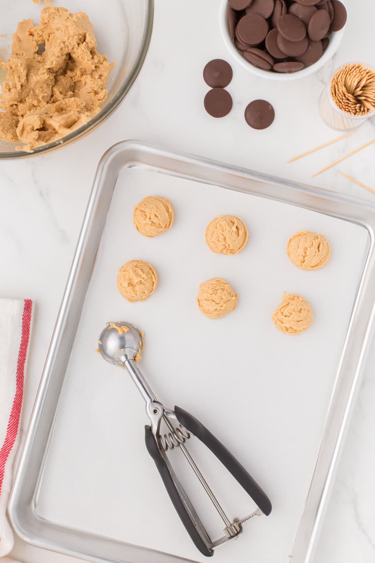 overhead shot showing buckeye peanut butter balls being dropped onto a wax paper-lined baking sheet with a 1-tablespoon cookie scooper