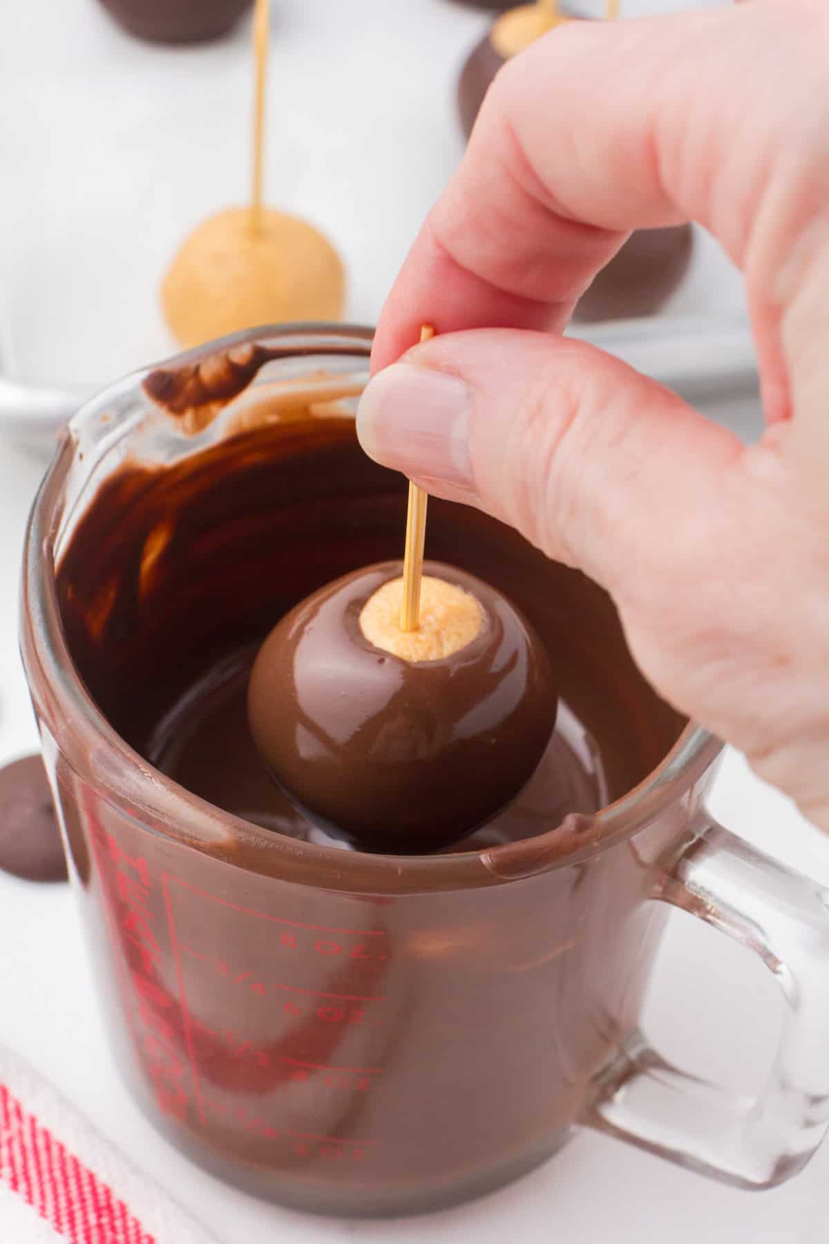 using a toothpick to dip buckeye balls in melted chocolate in a microwave-safe glass measuring cup