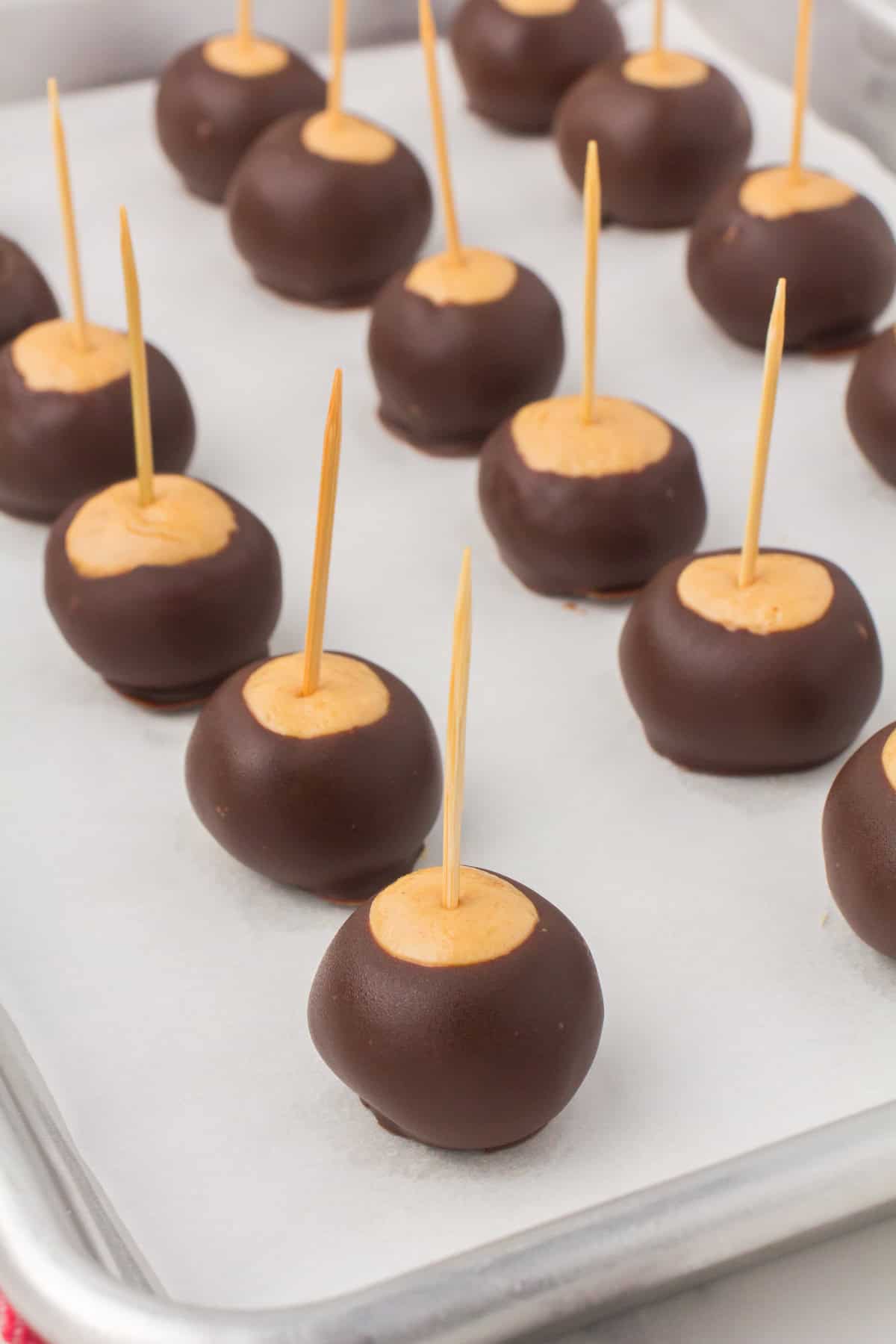freshly dipped buckeye balls with toothpicks laid out on a wax paper-lined baking sheet
