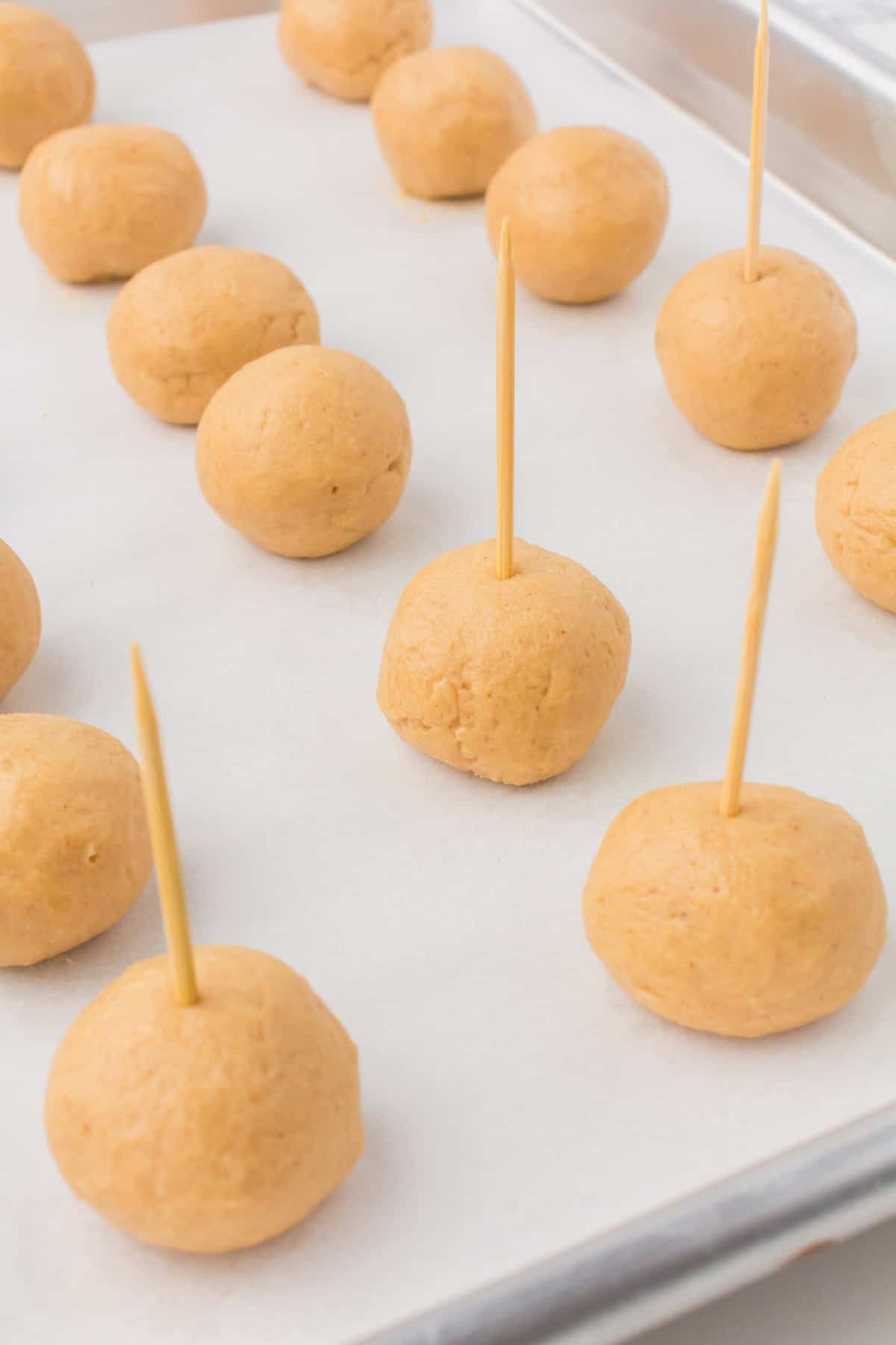 buckeye peanut butter balls with toothpicks in the top set out on a wax paper-lined baking sheet ready to dip