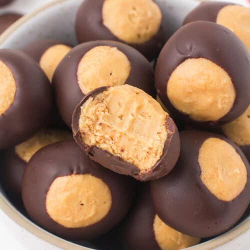closeup of buckeye peanut butter balls heaped up in a small gray bowl with a bite taken out of one on the top
