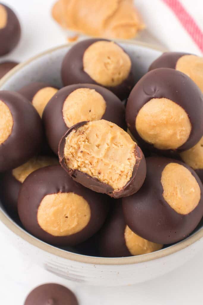 closeup of buckeye peanut butter balls heaped up in a small gray bowl with a bite taken out of one on the top