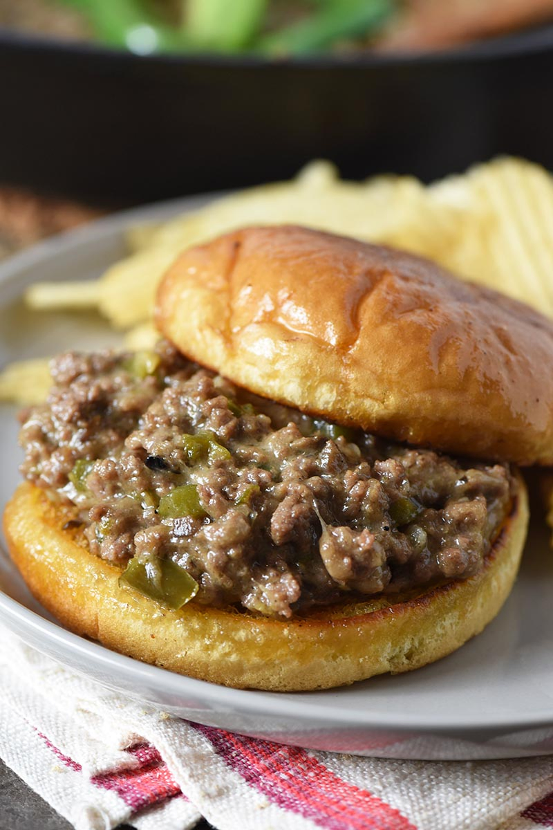 close up of Philly cheesesteak sloppy joes on gray plate with toasted hamburger bun and potato chips