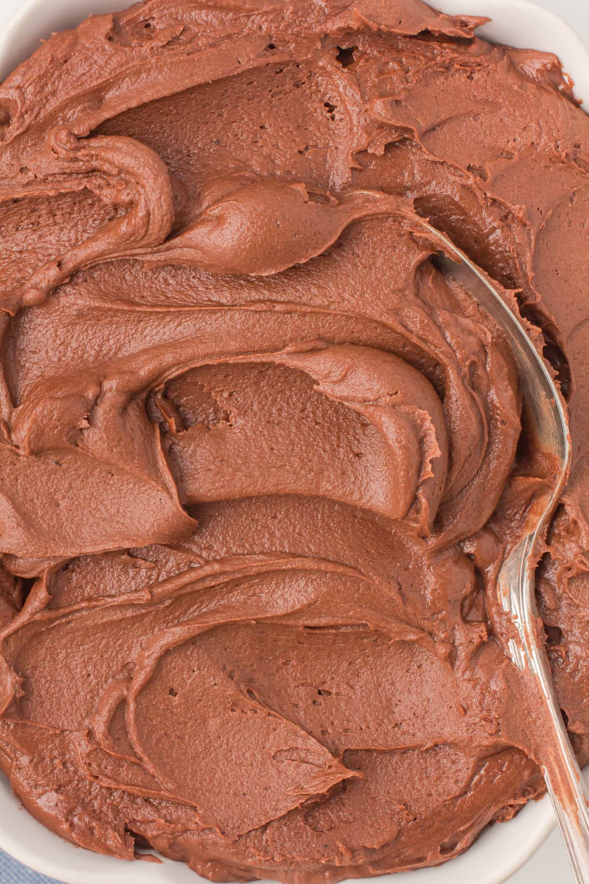 closeup overhead shot showing chocolate buttercream icing in a large white bowl with a spoon