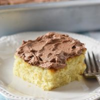 slice of yellow cake with chocolate buttercream frosting on an ivory plate with a fork