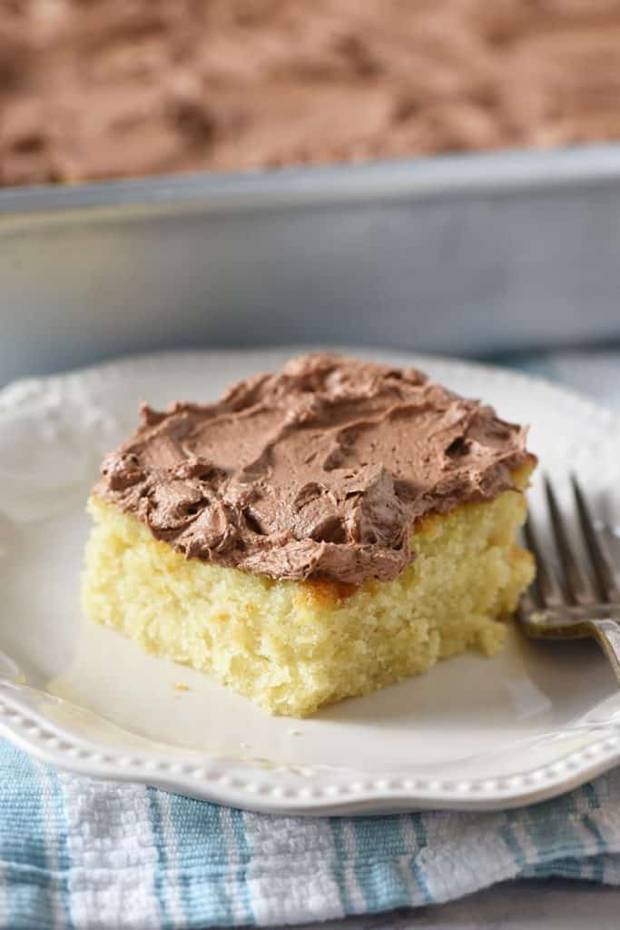 slice of yellow cake with chocolate buttercream frosting on an ivory plate with a fork
