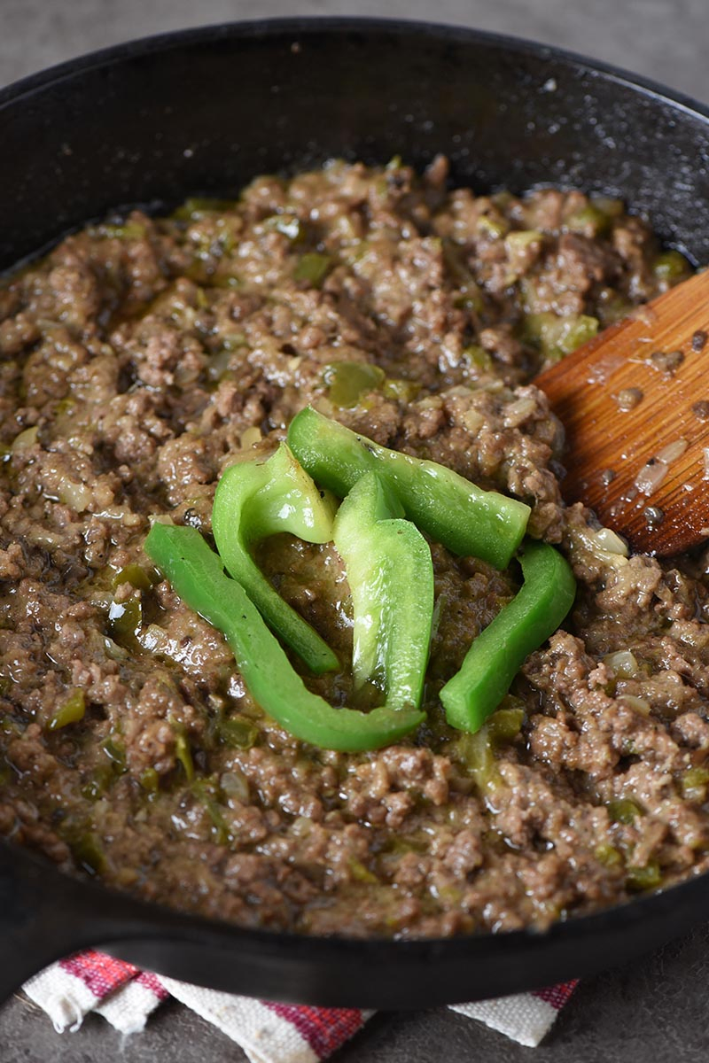 ground beef for Philly cheesesteak sloppy joes, cooked in cast iron skillet with green bell peppers and wooden spatula