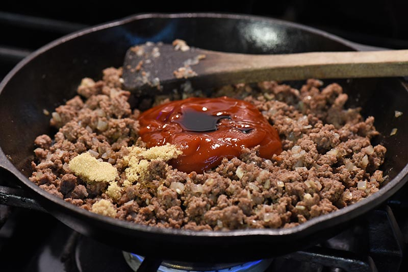 mixing sloppy joe sauce ingredients into ground beef mixture in cast iron skillet