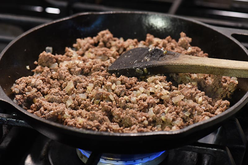 mixing onion, garlic, and ground beef together while making grilled cheese sloppy joe recipe in cast iron skillet