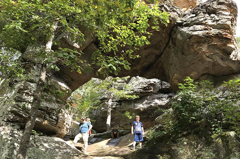 dad and sons posing with Natural Bridge on Arkansas hiking trail, Seven Hollows Trail, in Petit Jean State Park