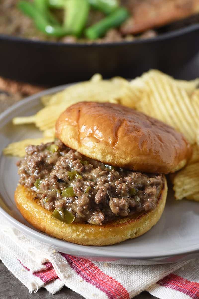 open faced Philly cheesesteak sloppy joes on toasted hamburger buns with potato chips on gray plate
