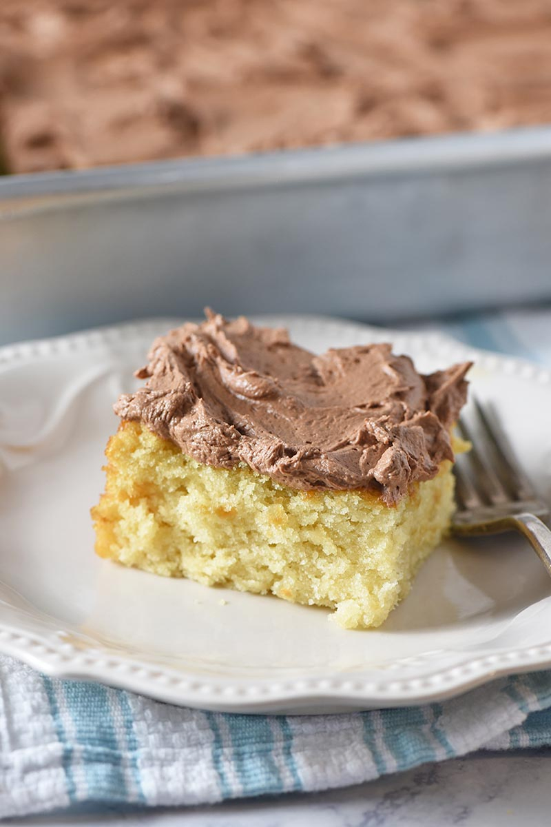 slice of yellow cake with chocolate frosting on white plate with fork