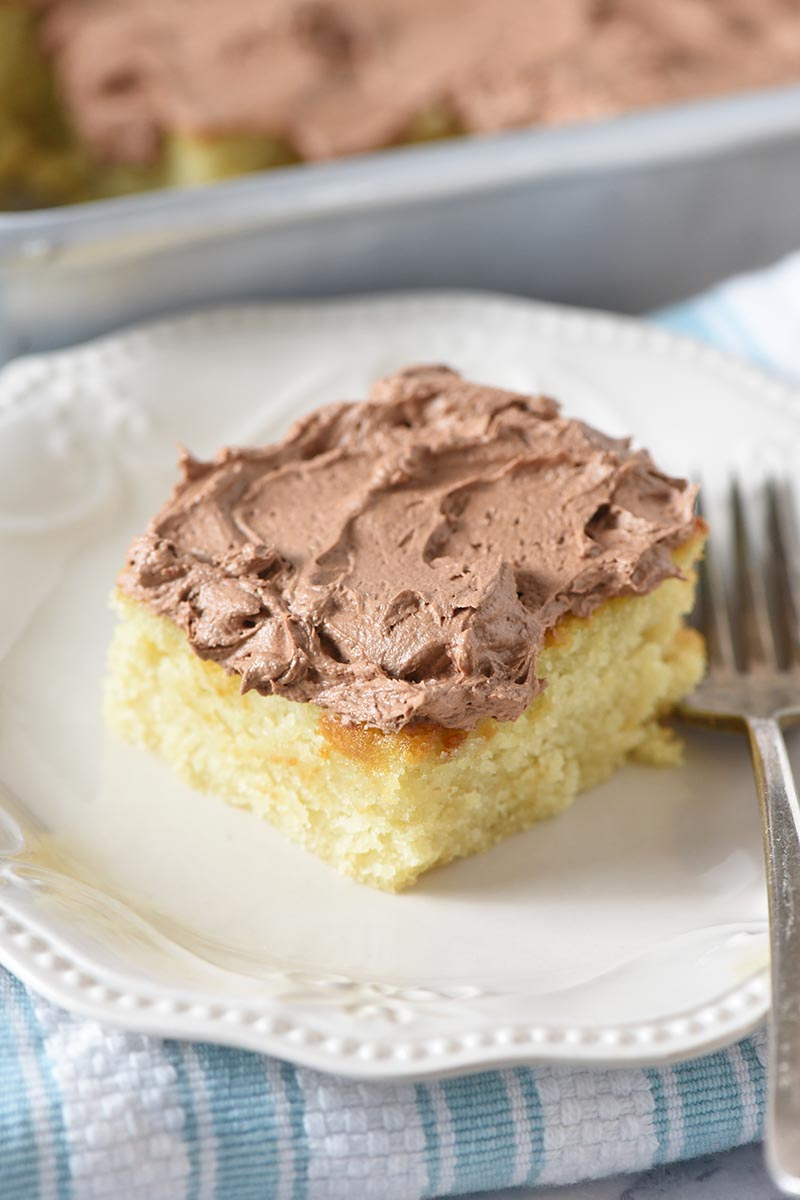piece of yellow cake with chocolate buttercream frosting on ivory plate with fork