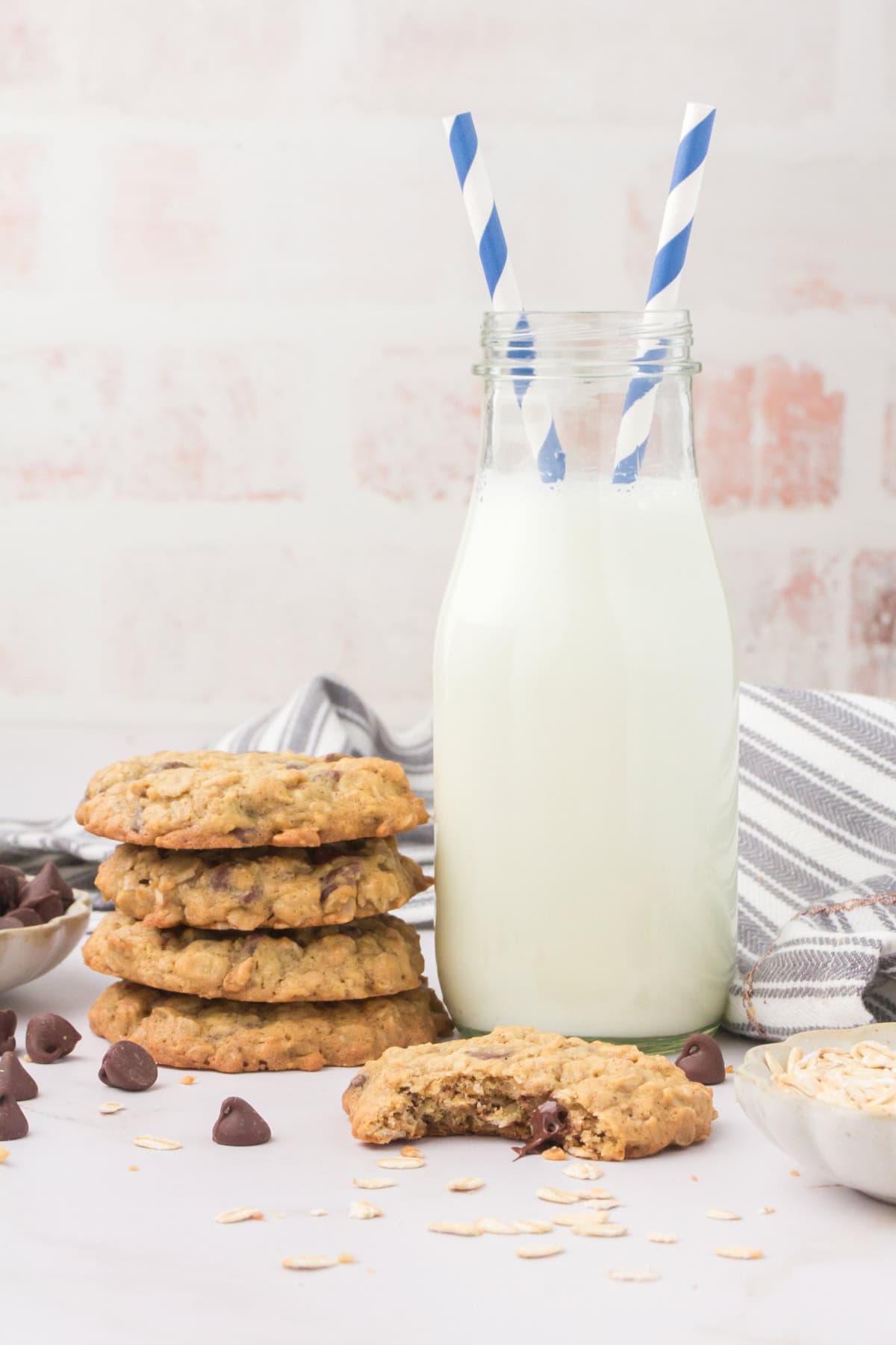 buttermilk oatmeal cookies stacked up next to a cold glass of milk with blue and white striped straws