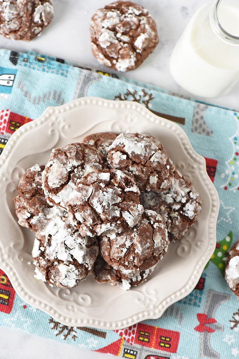 chocolate mint crinkles piled on plate with holiday kitchen towel and served with milk