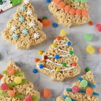 decorated Christmas tree Rice Krispie treats on white marble background with candies and holiday kitchen towel
