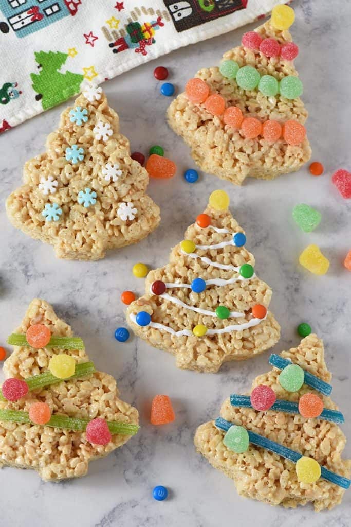 decorated Christmas tree Rice Krispie treats on white marble background with candies and holiday kitchen towel