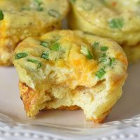 bite out of ham and cheese egg muffins on white plate