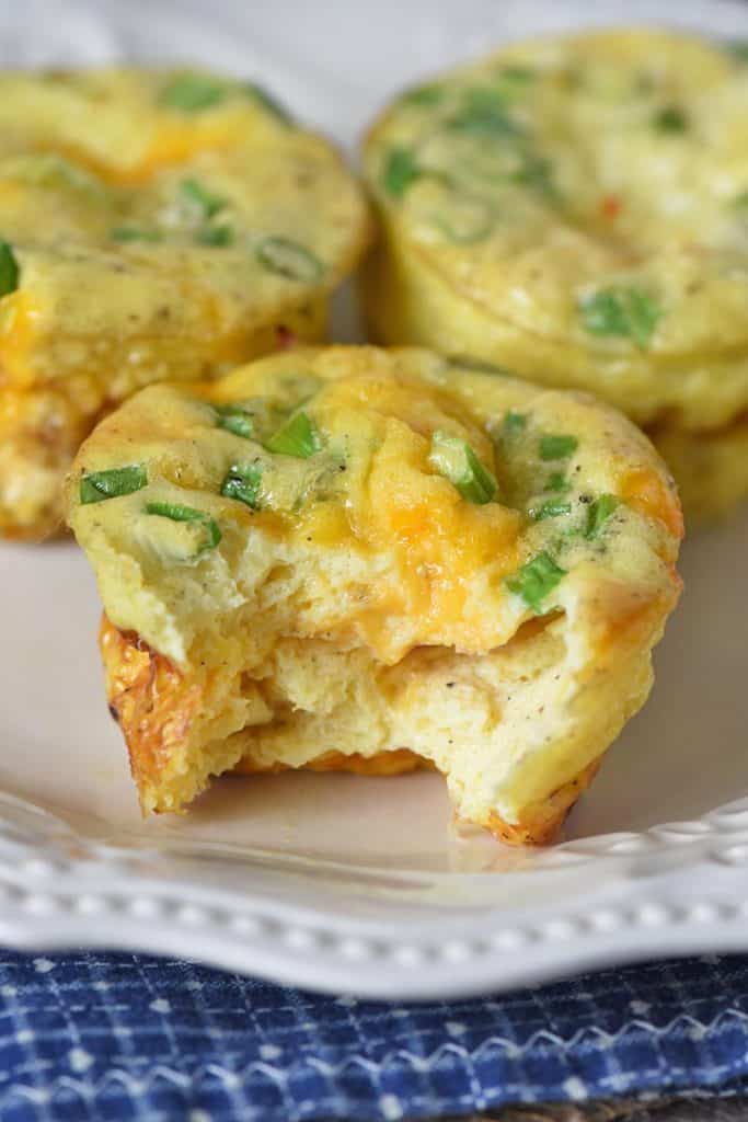 bite out of ham and cheese egg muffins on white plate