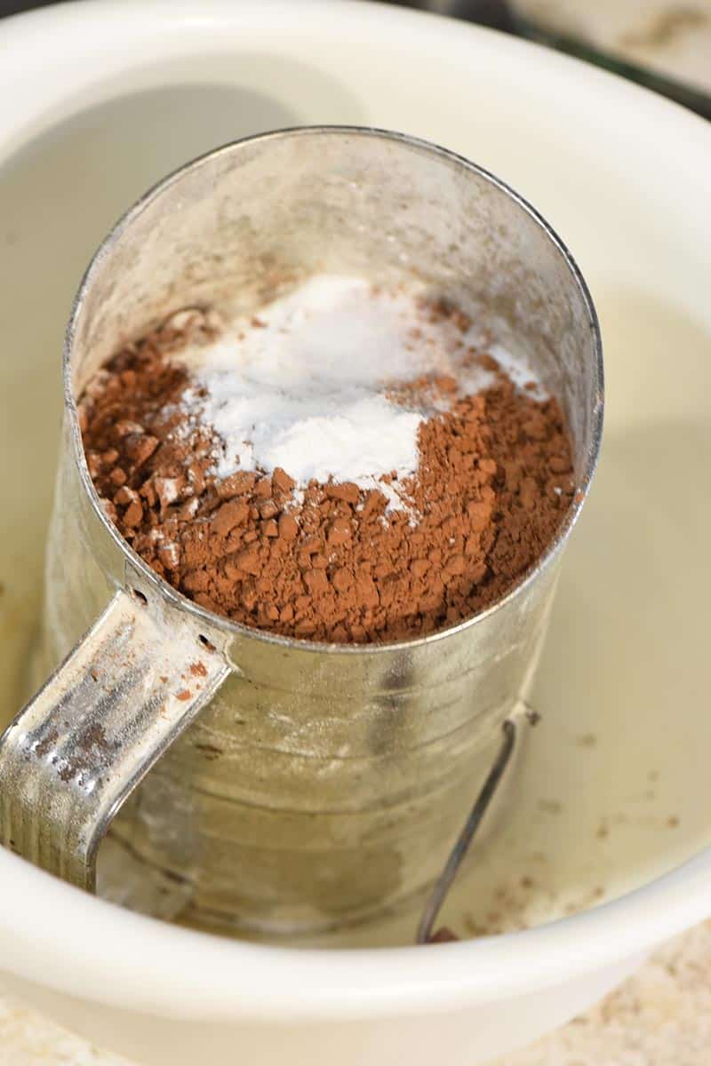 sifting together dry ingredients, including cocoa powder, for chocolate crinkle cookies