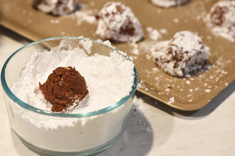 rolling chocolate crinkle cookies dough balls in powdered sugar for baking