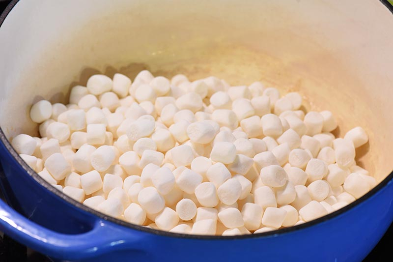 using mini marshmallows to make marshmallow treats in blue Dutch oven