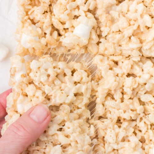 closeup shot showing gooey Rice Krispie square being pulled out of a pan full of Rice soft and chewy Krispie treats