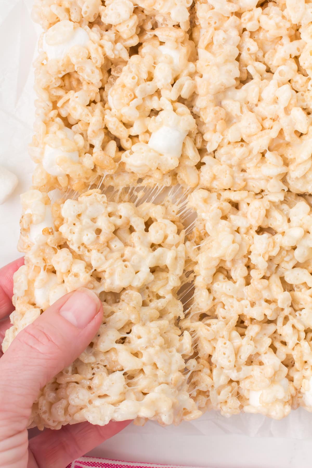 closeup shot showing gooey Rice Krispie square being pulled out of a pan full of Rice soft and chewy Krispie treats