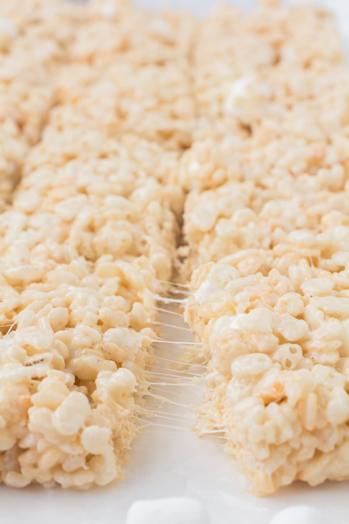 fresh batch of gooey Rice crispy treats with melted marshmallows pulled apart on a white countertop