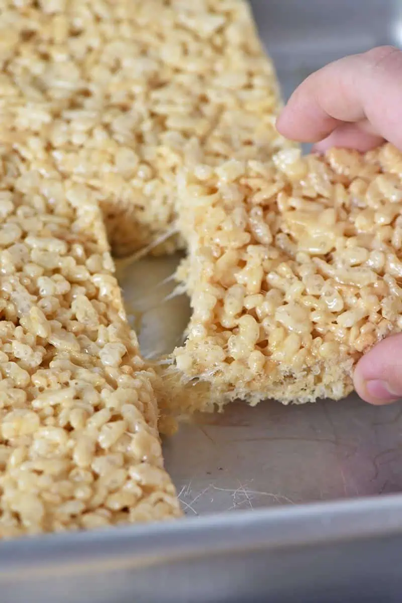 hand pulling Rice Krispie treats out of a metal cake pan