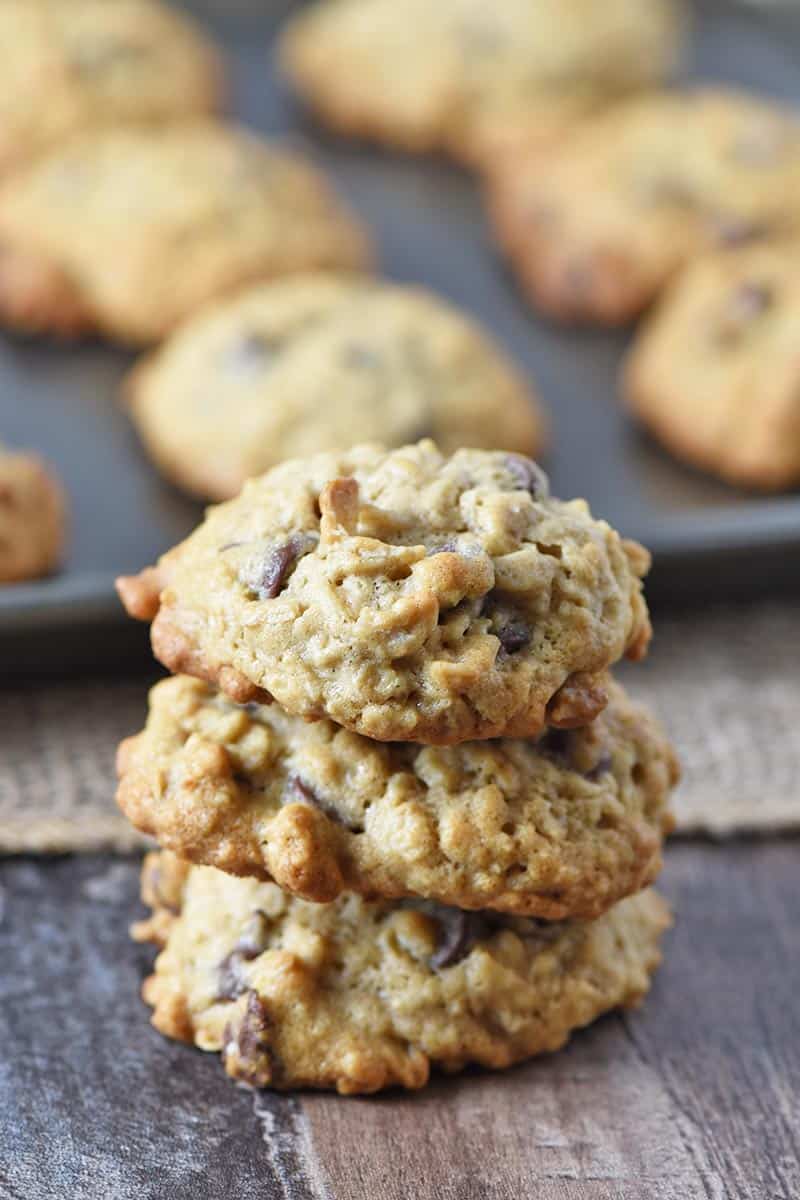 stack of oatmeal chocolate chip cookies on gray countertop with cookie sheet behind